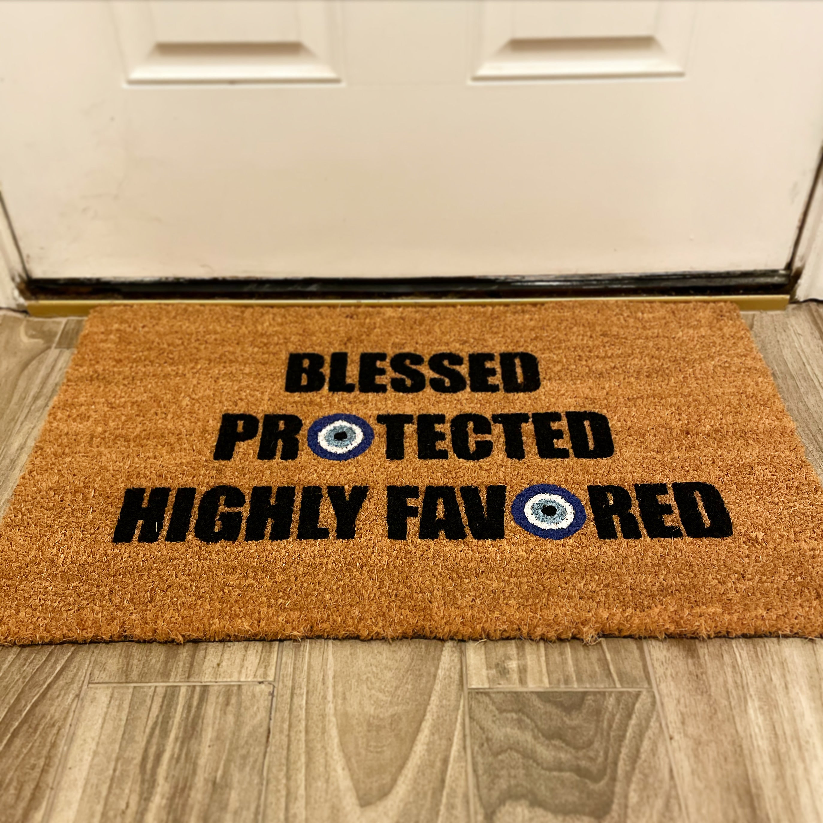 The Doormat District with 'Blessed Protected Highly Favored' text and blue evil eye designs. 