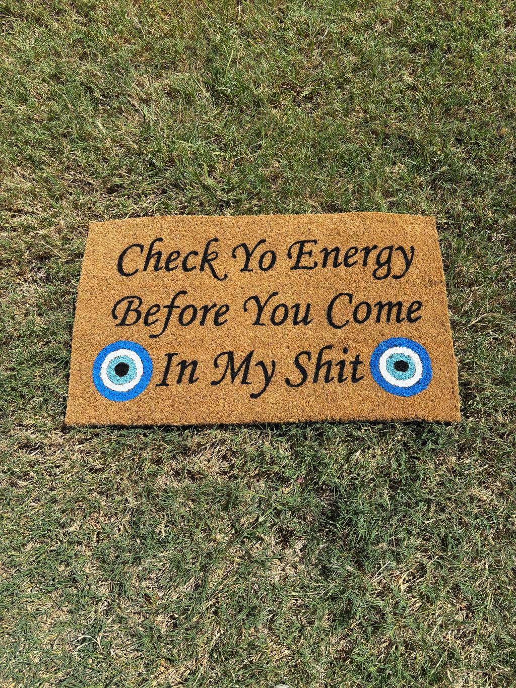 The Doormat District doormat that says "Check Yo Energy Before You Come In My Sht" with two blue evil eyes 