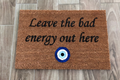 The Doormat District doormat with text "Leave The Bad Energy Out Here" with Blue Evil Eye