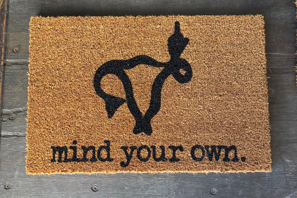 The Doormat District doormat with phrase "mind your own" with image of a Uterus