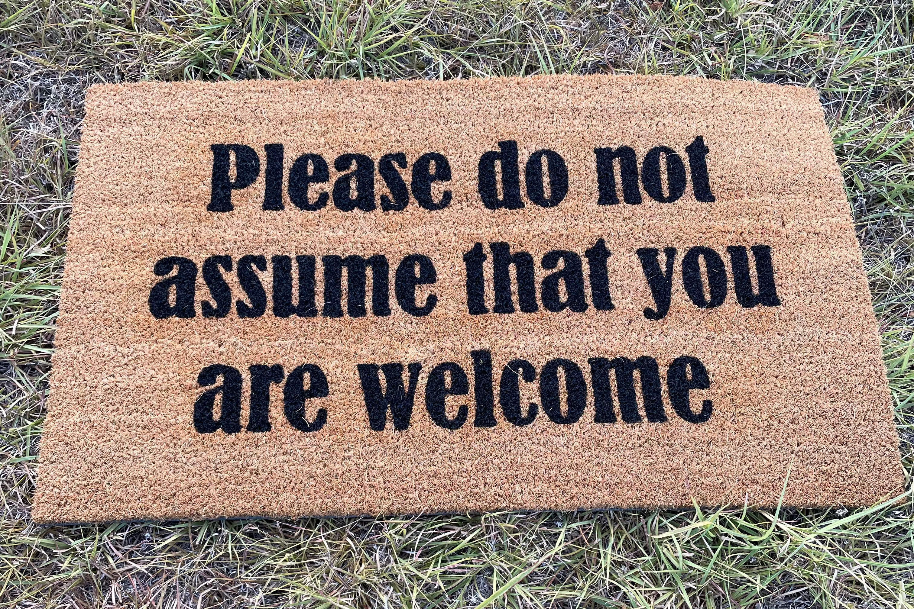The Doormat District doormat with text "Please Do Not Assume That You Are Welcome" 