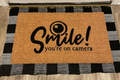The Doormat District doormat with text "Smile You're On Camera"