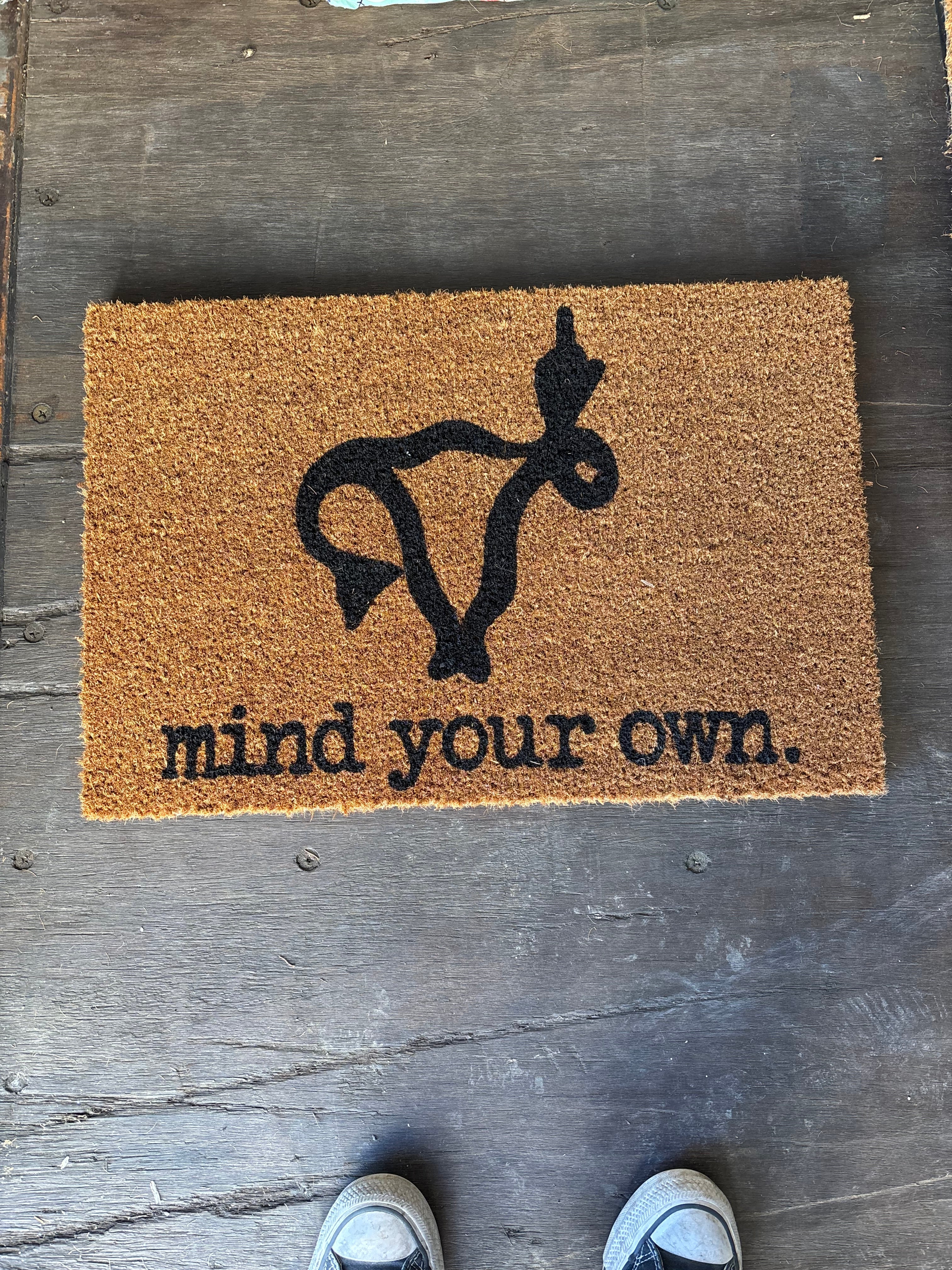 The Doormat District doormat with quote "Mind Your Own" with a uterus image